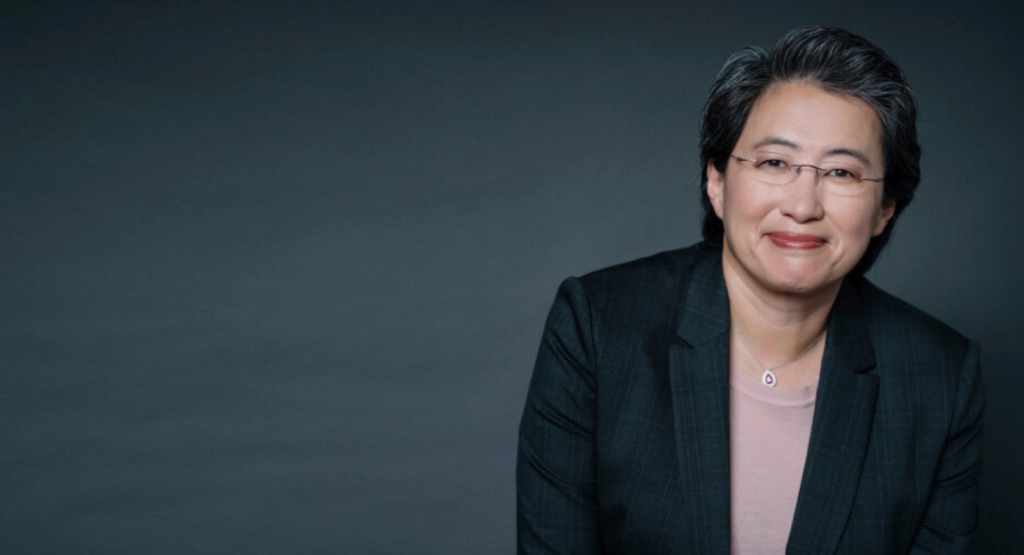 Professional portrait of Dr. Lisa Su, Chair and Chief Executive Officer of AMD, wearing a dark pinstripe blazer over a light pink top with a delicate necklace, against a dark gradient background.